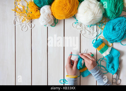 Una donna maglieria calze lavorate a maglia con bambini aghi di tessitura. strisce di turchese, giallo e bianco colori. Foto Stock