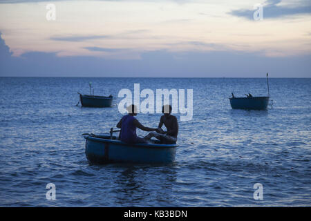 Vietnam, Mui NE, Mui NE Beach, pescatore in tipica barca da pesca 'Coracle', crepuscolo, Foto Stock