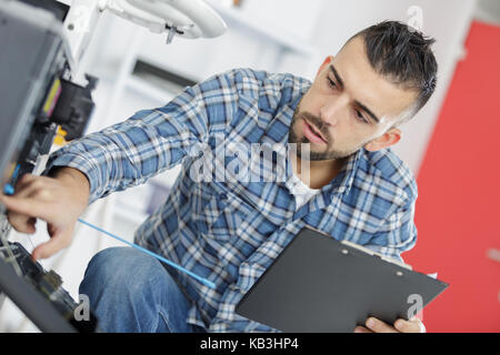 Tecnico maschile seduto vicino a lavastoviglie iscritto negli appunti in cucina Foto Stock