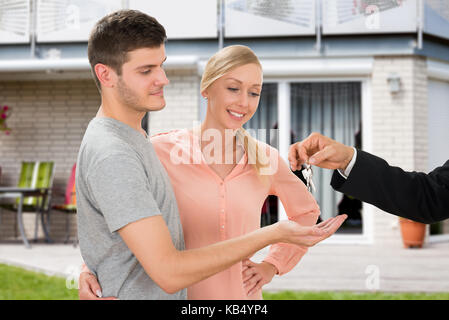 Close-up di agente dando chiave della nuova casa per la giovane coppia felice Foto Stock