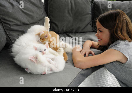 La ragazza si inginocchia davanti a nursing gatto sul divano grigio Foto Stock