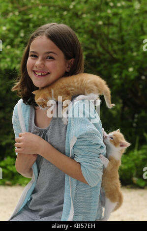 Ragazza con due gattini sulle spalle e risate nella fotocamera, alberi sullo sfondo sfocato Foto Stock