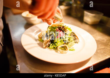 Lo chef di cucina è l'insalata di mare consisteva nella letuce, cozze e cerchi di cipolla collocato sulla piastra bianca. La vista laterale. Foto Stock