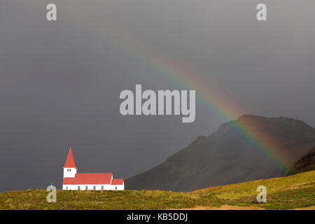 Chiesa e rainbow contro il cielo tempestoso e montagne, vik y myrdal, sud Islanda, regioni polari Foto Stock