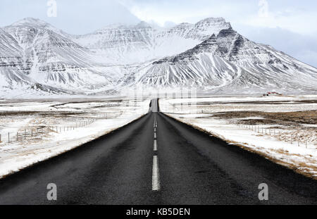 Nero su strada asfaltata che conduce verso montagne coperte di neve in inverno, sud Islanda, regioni polari Foto Stock