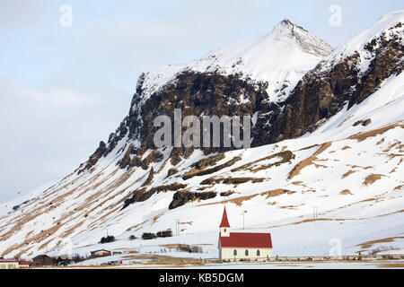 Il bianco e il rosso chiesa contro le montagne coperte di neve, vik, sud Islanda, regioni polari Foto Stock