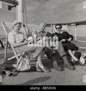 Degli anni Cinquanta, storiche, i passeggeri anziani a bordo di una nave Union-Castle sit in sedie a sdraio sul ponte la lettura di libri e rilassante. Foto Stock