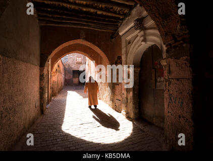 Local uomo vestito in djellaba tradizionale a piedi attraverso archway in una strada nella Kasbah, Marrakech, Marocco, Africa del nord Foto Stock