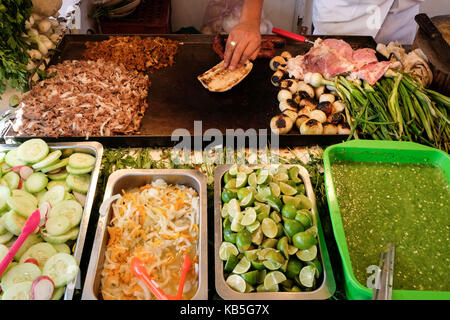 Un uomo si prepara il cibo in un luminoso e colorato taqueria stand su una strada laterale a Città del Messico. Foto Stock