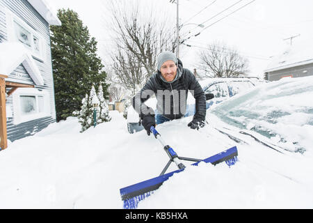 L'uomo spazzolando la neve fuori dal parabrezza della sua automobile Foto Stock