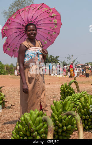 Una signora la vendita delle banane al mercato ripari dal sole sotto un ombrello rosa, Ruanda, Africa Foto Stock