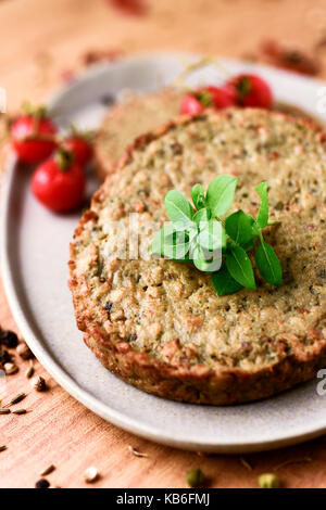 Primo piano di alcuni veggie hamburger di melanzane e altre verdure in una piastra, posto su una tavola in legno rustico Foto Stock