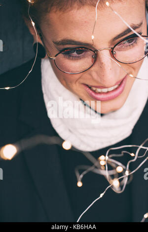 Giovani redhead donna che indossa abbigliamento invernale e tenendo le luci di Natale Foto Stock