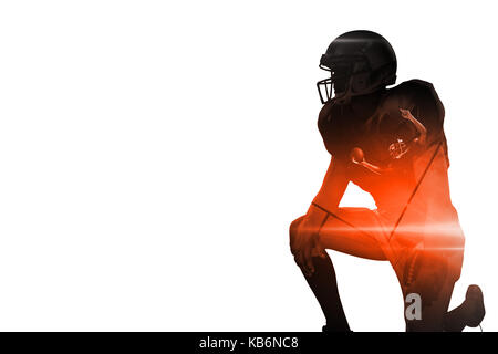 Giocatore di football americano che guarda lontano mentre inginocchiato contro lo sfondo nero Foto Stock