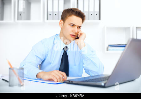 Ritratto di giovane imprenditore pensieroso parlando al cellulare in ufficio Foto Stock