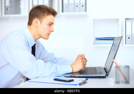 Vista laterale giovane imprenditore lavorando sul computer portatile in ufficio luminoso Foto Stock