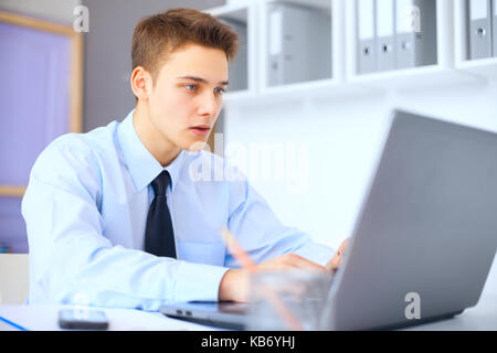 Giovane imprenditore gravi lavorando sul computer portatile in ufficio luminoso Foto Stock