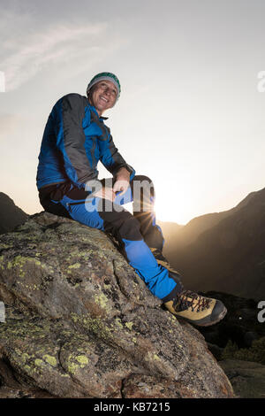 Bella giovane escursionista prendendo una pausa su una pietra e gode il sunrise nelle montagne svizzere Foto Stock