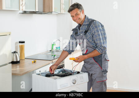 Per tutta la lunghezza del tecnico di controllo della macchina di lavaggio con multimetro digitale in cucina Foto Stock