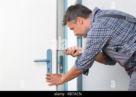 Immagine ritagliata del tecnico il fissaggio serratura di porta con un cacciavite a casa Foto Stock