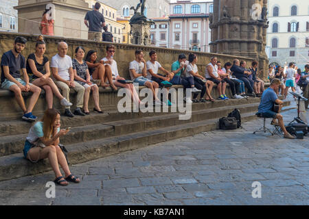 Italia, Toscana, Firenze, Piazza della Signoria, in estate. Turisti che si rompono dal caldo seduto all'ombra , ascoltando un busker Foto Stock