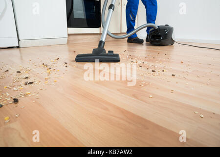 Sezione bassa di bidello maschio piano di pulizia con aspirapolvere in cucina Foto Stock