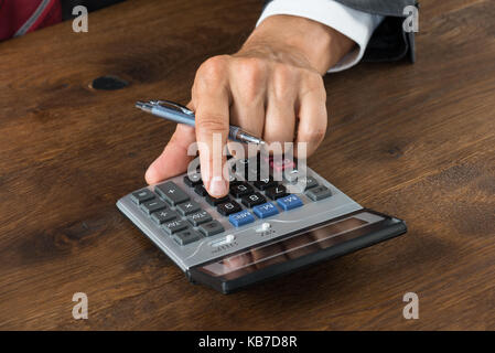 Immagine ritagliata di imprenditore utilizzando la calcolatrice a scrivania in legno Foto Stock