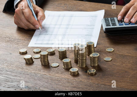 Immagine ritagliata di imprenditore il calcolo del profitto con le monete sulla scrivania Foto Stock