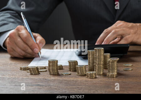 Immagine ritagliata di ragioniere calcolare il profitto con le monete sulla scrivania Foto Stock