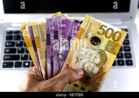 Foto di una mano che tiene il denaro e un computer portatile Foto Stock