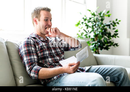 Scioccato uomo con alcuni documenti sul divano livingroom Foto Stock