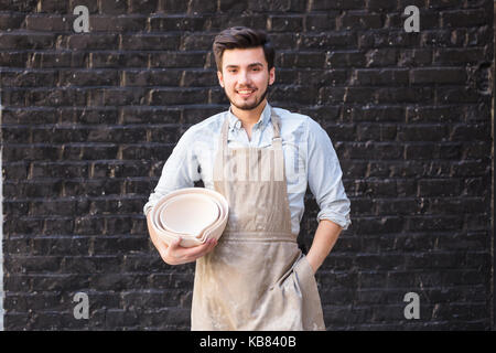Vasellame, utensili, arte ceramica concetto - sorridente ceramista maschio con mani tenendo alcune bocce, carino finito di prodotti di argilla e felice artigiano sul Foto Stock