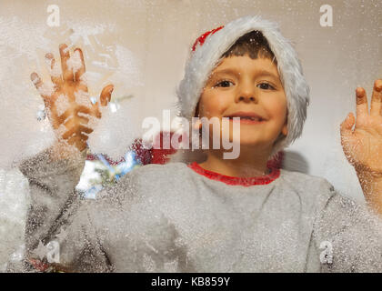 Ragazzo nel cappello di Natale decorato con finestra congelati Foto Stock