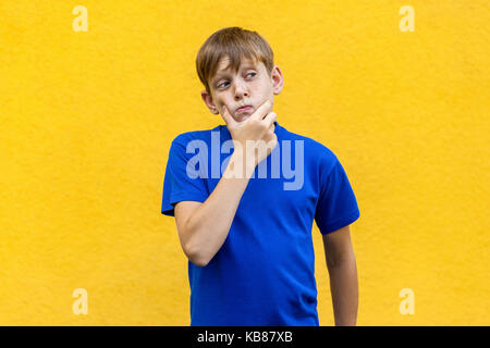 Riflessivo Ragazzo che guarda lontano mentre in piedi contro sfondo giallo. studio shot Foto Stock