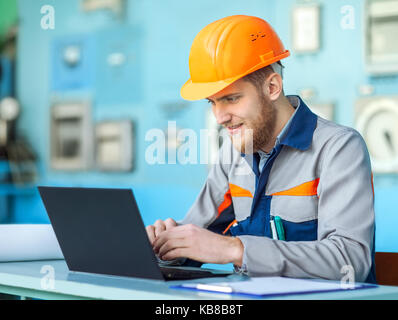 Ritratto di giovane ingegnere Felice lavorando al computer portatile in sala di controllo Foto Stock