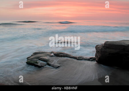 Una lunga esposizione seascape di rottura onde lungo la rocciosa la jolla costa in san diego california prese durante un drammatico tramonto colorato. Foto Stock