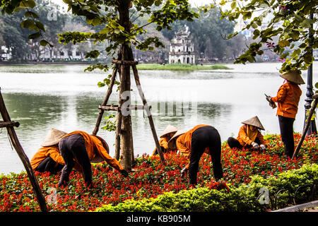 Le donne tendono fiori nella parte anteriore del Thap Rua tempio o torre di tartaruga, lago Hoan Kiem, Hanoi, Vietnam Foto Stock