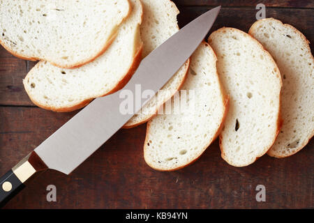 Fette di pane bianco e coltello da cucina sulla superficie di legno Foto Stock