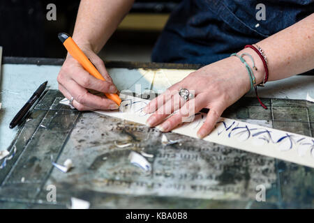 Un'artista utilizza un mestiere coltello per tagliare un sollievo da una striscia di linoleum per la stampa. Foto Stock