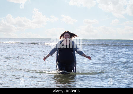 Una bella donna che cammina fuori dell'oceano con un grande sorriso e le braccia spalancate Foto Stock