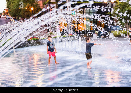 Washington DC, Stati Uniti d'America - 4 Agosto 2017: ragazzi giovani bambini che giocano in acqua fontana in Georgetown Waterfront Park in serata con spruzzi d'acqua Foto Stock