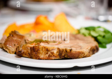 Deliziosa bistecca di carne di maiale con golden patate al forno e insalata su piastra bianca Foto Stock