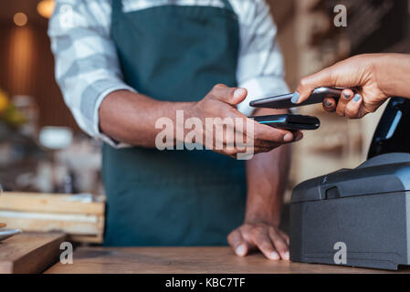 Il cliente utilizza il suo smartphone per pagare il suo cafe acquisto Foto Stock