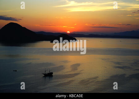 Orange sunrise vista da isola padar parte del parco nazionale di Komodo con piccola barca silhouette nell'oceano, flores indonesia. Foto Stock