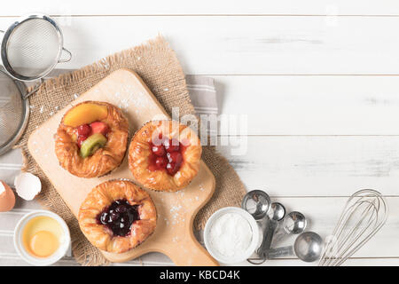Pane danese con frutti, mirtillo e ciliegia salsa e apparecchiature su bianco sullo sfondo di legno, prodotti alimentari da forno Foto Stock