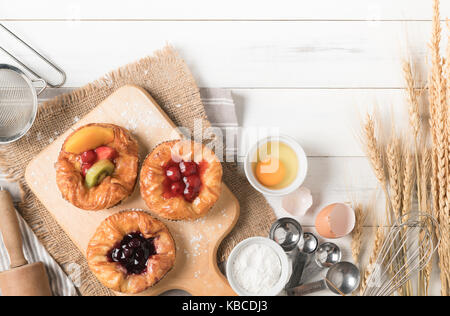 Pane danese con frutti, mirtillo e ciliegia salsa e apparecchiature su bianco sullo sfondo di legno, prodotti alimentari da forno Foto Stock