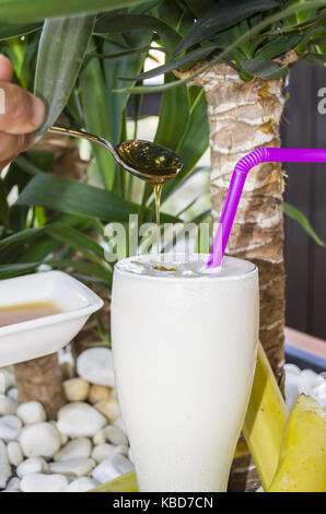 Frullato di banana con miele in un bicchiere è posto sulla pietra bianca sullo sfondo Foto Stock