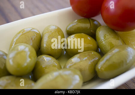 Verde Verde Oliva piastra; su di un tavolo di legno con le fette di limone e i pomodori ciliegia Foto Stock