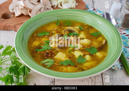 Una sana zuppa di grano saraceno, di fecola di patate, funghi, carote e cipolla oliva wit oi in una ciotola verde su uno sfondo di legno Foto Stock