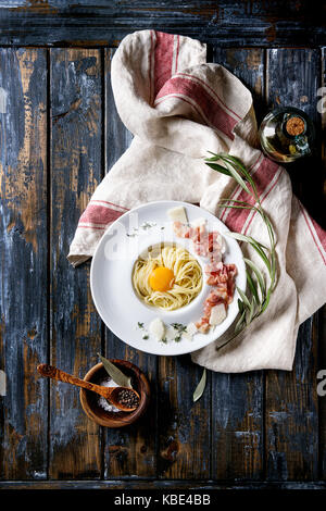 Tradizionale italiana la pasta alla carbonara con tuorlo d'uovo, pancetta, parmigiano, timo, servita nella piastra bianca sul tessile su un vecchio ceppo di legno bac Foto Stock